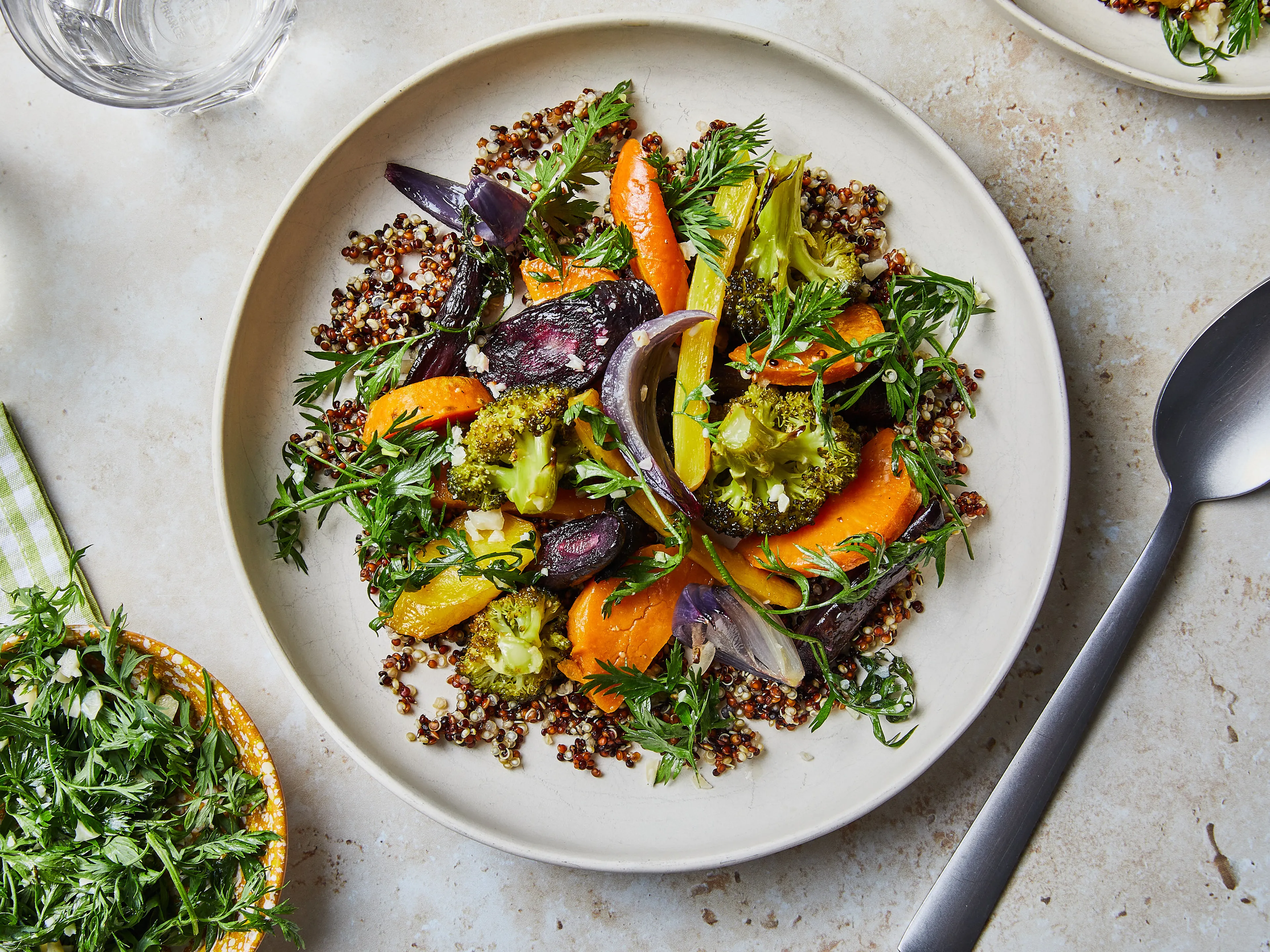 A grain bowl with roasted vegetables, leaves and a spoon of dressing in a shallow dish