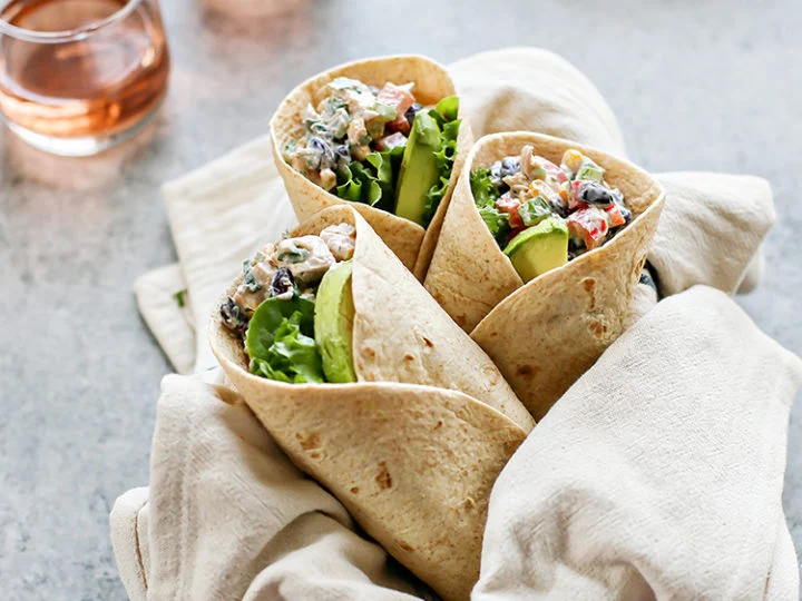 A folded wrap cut in half on a plate, showing layered fillings of beans, leaves and yoghurt